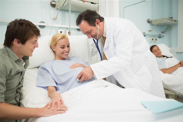 Obstetrician using a stethoscope on his smiling pregnant patient