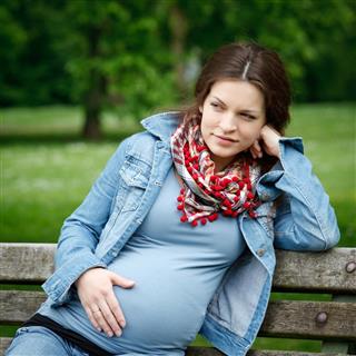 A pregnant woman sitting on a park bench