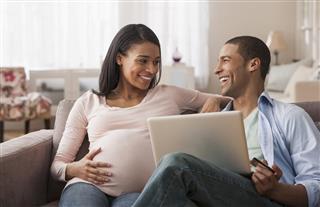 Young pregnant woman sitting with husband and laptop