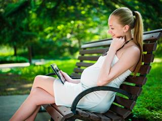 Pregnant woman in park with digital tablet