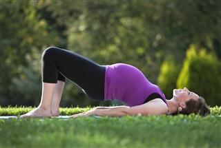 Pregnant Woman Practicing Yoga Bridge Pose Outdoors