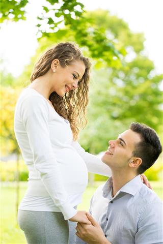 Happy and young pregnant couple in park in summer