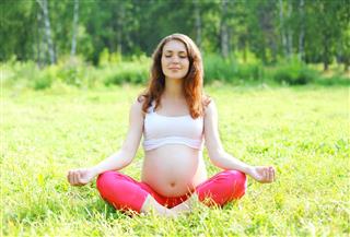 Young pregnant woman sitting on grass doing yoga exercise