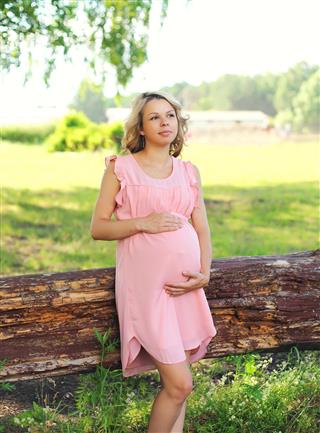 Pretty pregnant woman in pink dress outdoors on nature