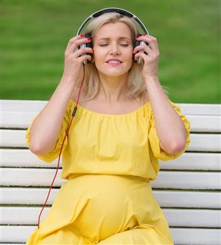 Pregnant girl in a yellow dress clothes headphones