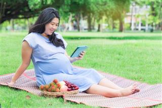 Pregnant woman with tablet relaxing in the garden