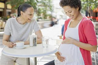 Pregnant woman holding stomach at cafe with friend