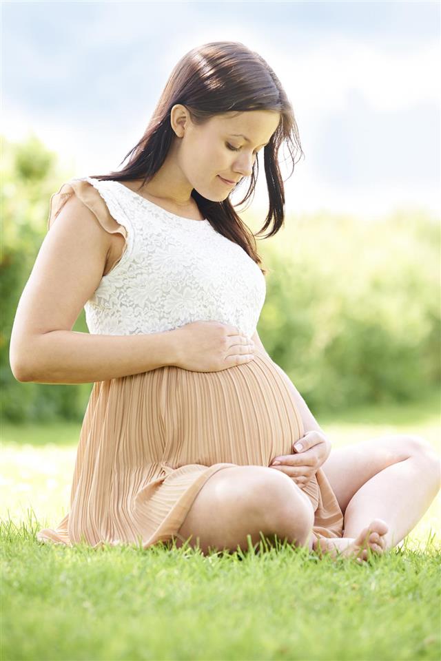 Pregnant Woman Sitting On Grass Outdoors Holding Bump