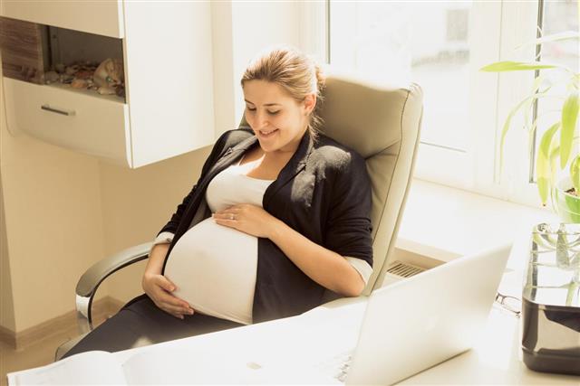 Businesswoman expecting for baby posing on chair at office