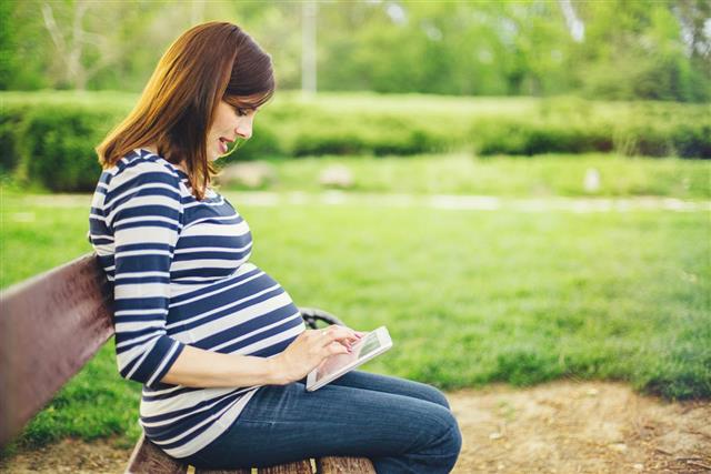 Pregnant woman reading about pregnancy on tablet