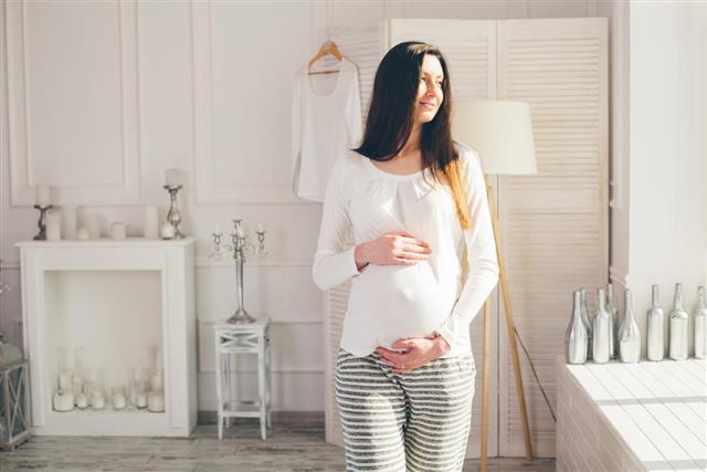 Pregnant woman at home walking and holding belly