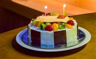 Round Fruit cake with chocolates and lit candles