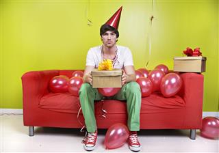 Sad Man Wearing Party Hat Holding Present with Balloons