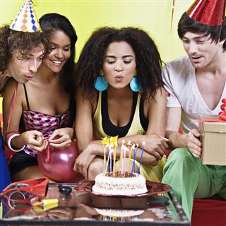 Young Woman Blowing Candles on Birthday Cake Celebrating with Friends