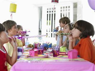 Children Blowing Party Puffers At Table