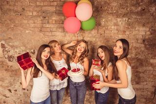 Smiling girls have party with presents, cake and balloons