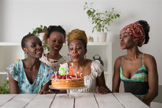 Girl looking at birthday cake surrounded by friends