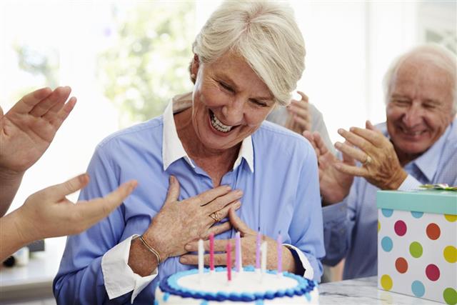 Senior Woman Blows Out Birthday Cake Candles At Family Party