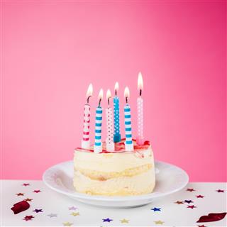 Birthday cake with candles standing on the table, pink background