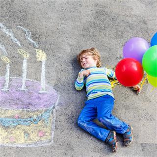 Kid boy with colorful chalks birthday cake and balloons