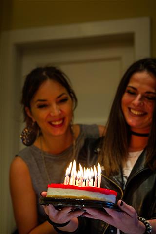 Two beautiful, happy girls, celebrating birthday, holding cake