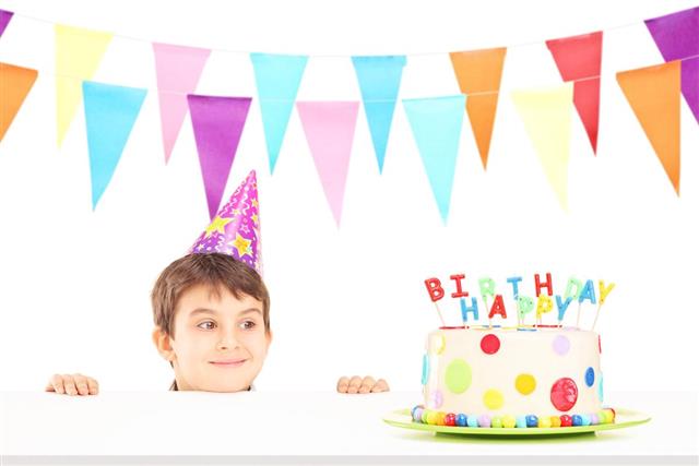 Smiling boy with party hat looking at a birthday cake