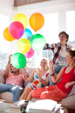 Friends With Balloons Sitting On Sofa In Living Room