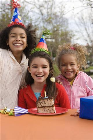 Girls (5-10) wearing party hats, slice of cake on table