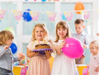 Smiling little girls with birthday cake and balloon