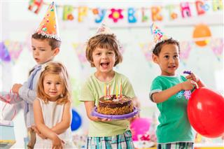 Cheerful birthday boy holding a cake at birthday party
