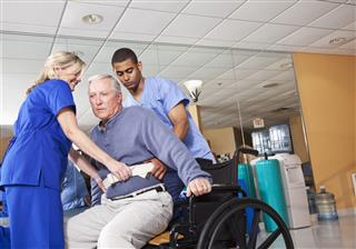 Healthcare Workers Helping Patient Into Wheelchair