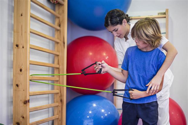 Physiotherapist Assisting Boy With Resistance Band