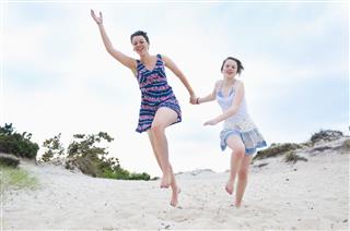 Woman And Girl Running On Beach