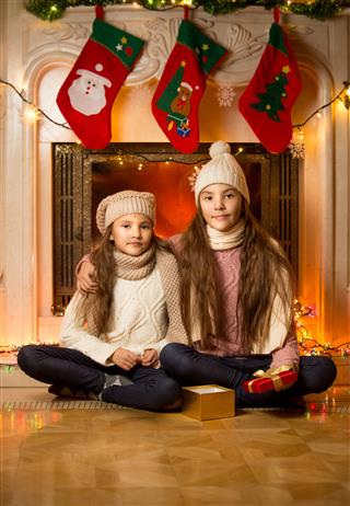 Cute Girls Sitting Next To Decorated Fireplace