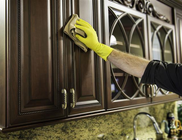 Man Cleaning Wooden Kitchen Cabinet