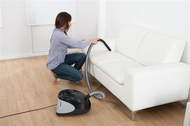 Young Woman Vacuuming Sofa At Home
