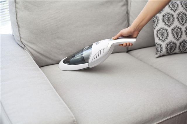 Woman With Vacuum Cleaning On Sofa