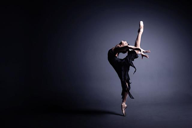 Young Ballerina In A Black Suit Is Dancing In Dark
