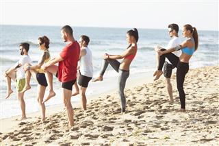 Group Exercising On Beach With Instructor