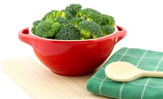 Red bowl with broccoli and wooden spoon on tea towel