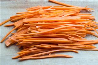 Raw strips sliced carrot on wooden cutting board