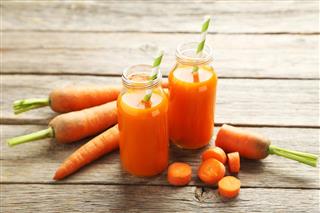 Fresh carrot juice in bottles on a gray wooden table