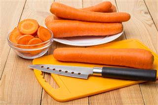 Raw carrots, cutting board and knife on table