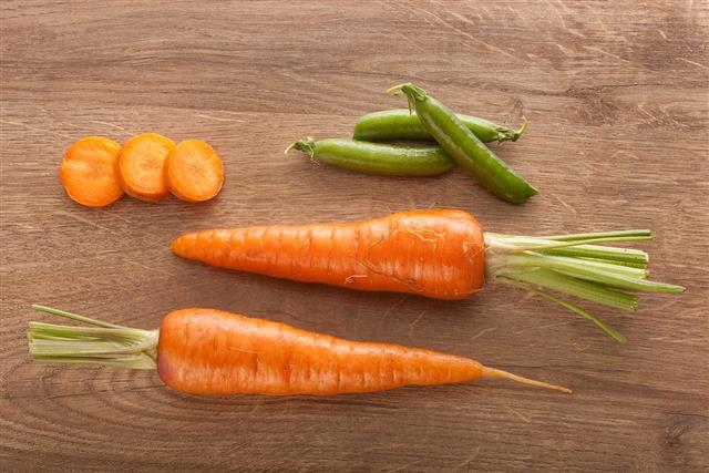 Carrot, carrot's slices and pea pods on the wood