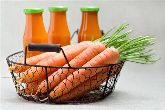 Three bottles of carrot juice and carrots in the basket