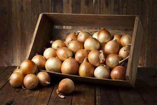Gold onions in a crate on rustic wood table
