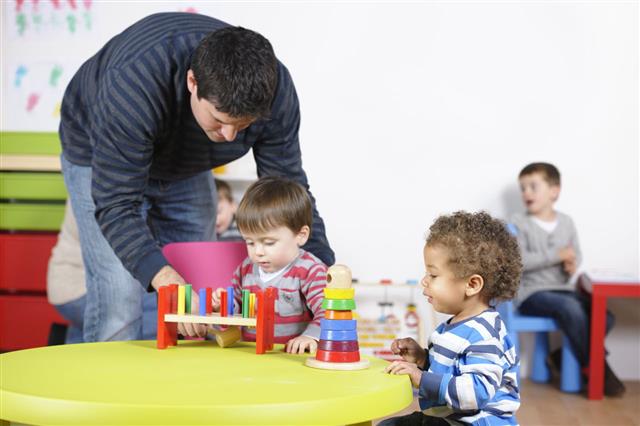 Carer Childminder Supports Toddler During Playtime In A Nursery Setting