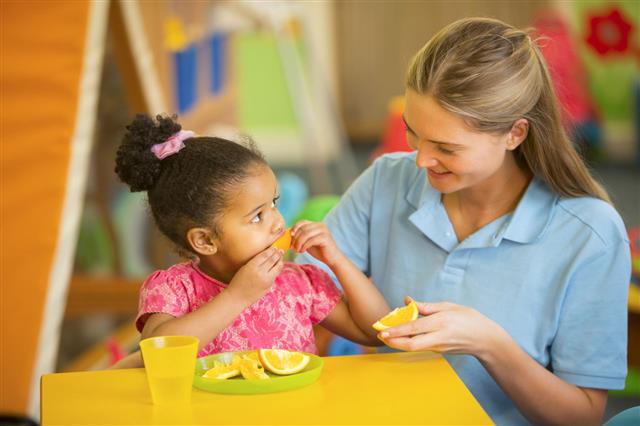 Nursery Teacher And Child Eating Oranges