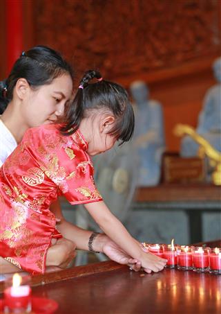 Mother And Girl Lighting Worship Candles