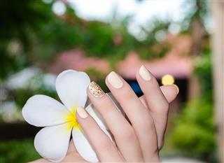 White plumeria in female hand with bright yellow nail design